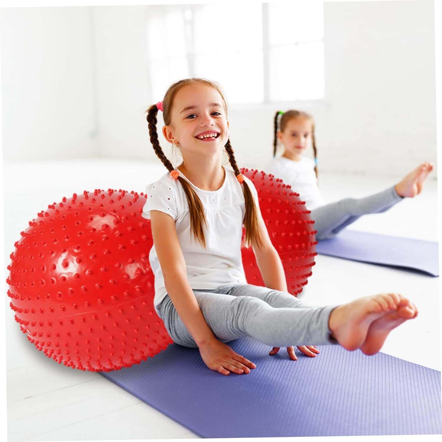 Niña jugando en una colchoneta con la pelota inflable EsencialLuz AlmaBalance para estiramientos y ejercicios.