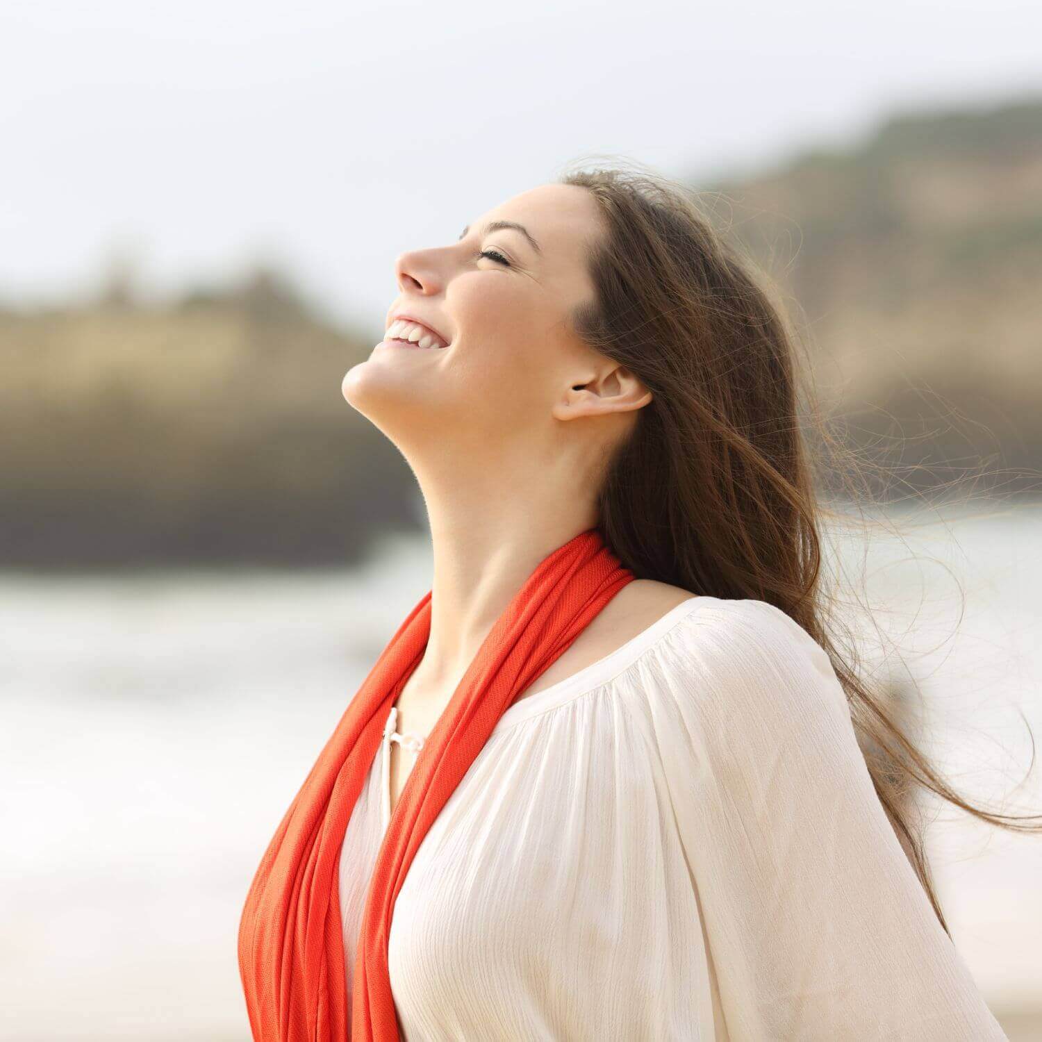 Mujer sonriendo en la playa, luce un look fresco y natural con su bufanda roja.