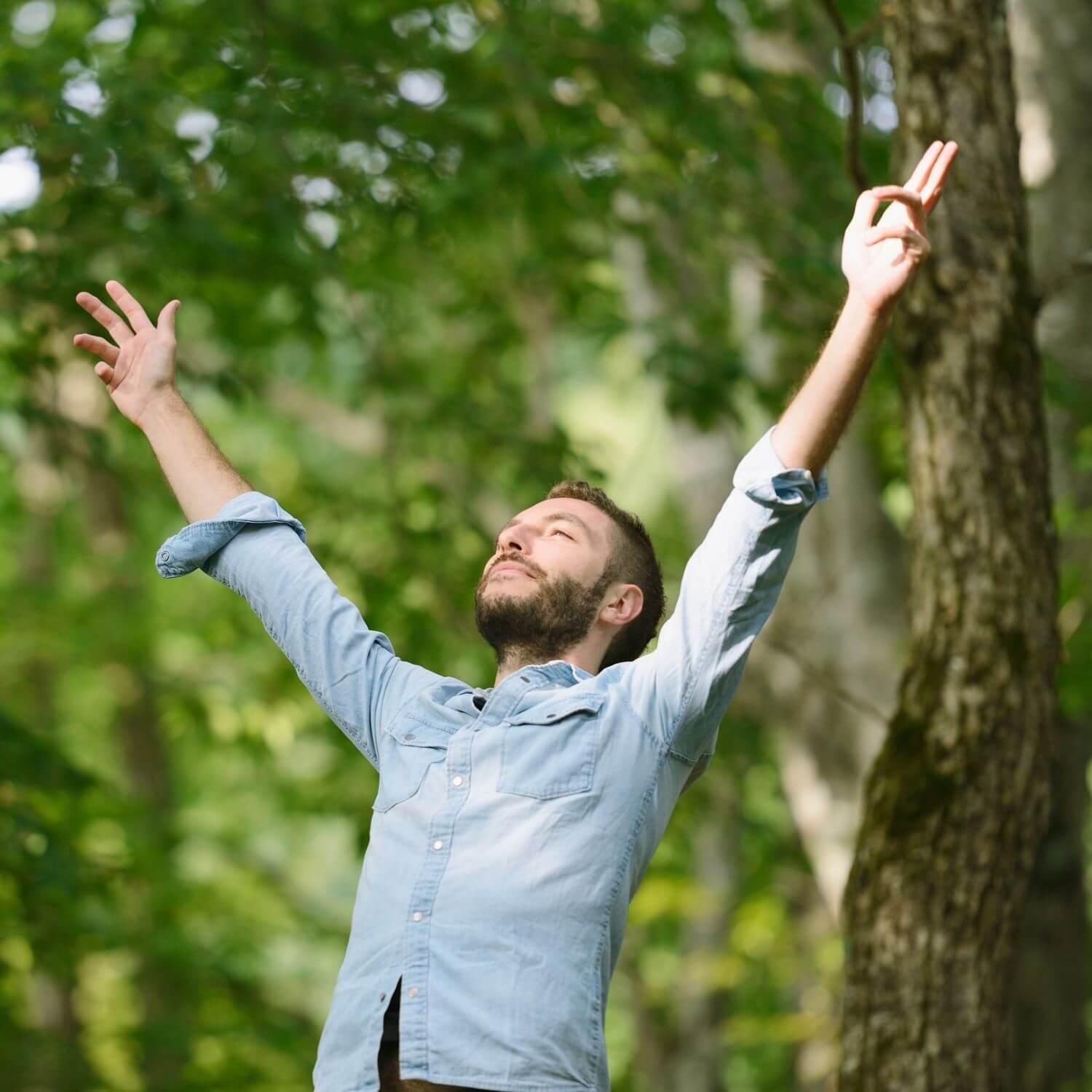 Hombre sonriente en la naturaleza levantando los brazos, disfrutando del momento al aire libre.